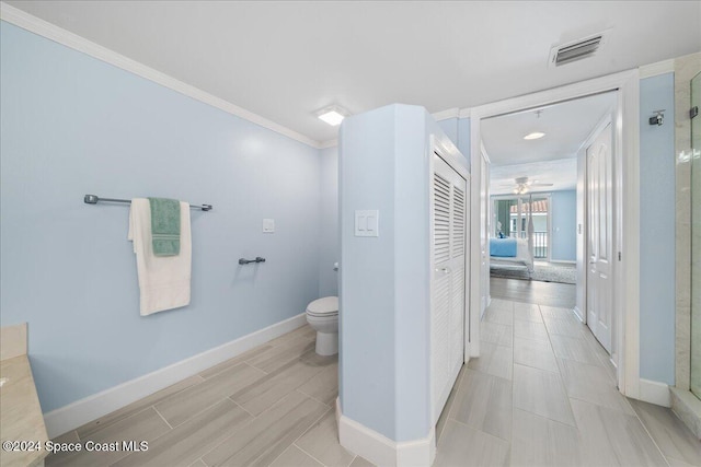 bathroom featuring ceiling fan, toilet, a shower with door, and crown molding