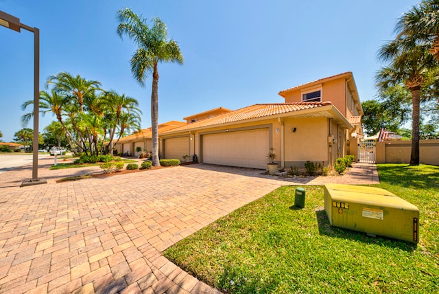 mediterranean / spanish-style house with decorative driveway, stucco siding, an attached garage, a gate, and a tiled roof