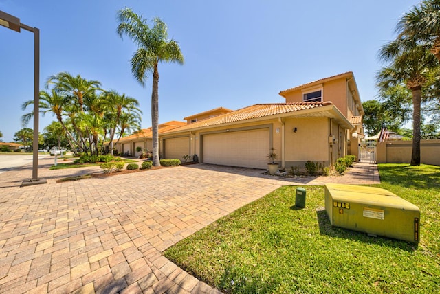 mediterranean / spanish-style home featuring a garage, a tile roof, decorative driveway, a gate, and stucco siding