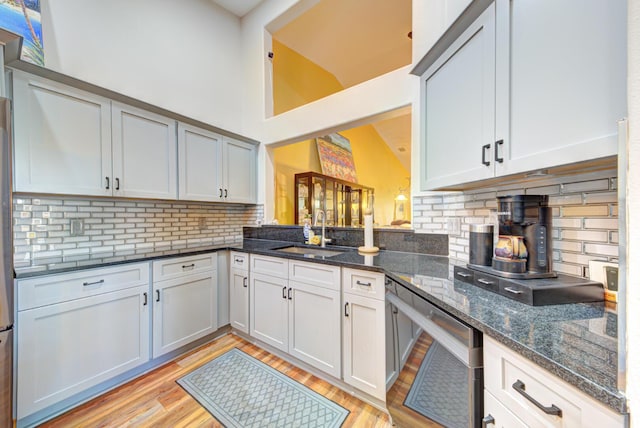 kitchen featuring a sink, tasteful backsplash, light wood-type flooring, dark stone counters, and white cabinetry