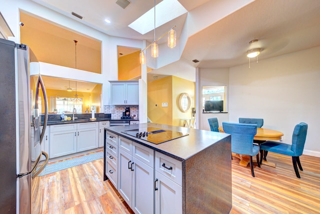 kitchen with a center island, stainless steel refrigerator with ice dispenser, black electric cooktop, decorative light fixtures, and light hardwood / wood-style floors