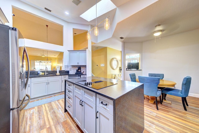 kitchen with stainless steel fridge, dark countertops, light wood-style floors, black electric cooktop, and pendant lighting