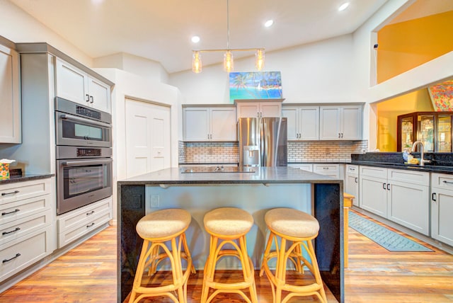 kitchen with a kitchen breakfast bar, light wood-type flooring, tasteful backsplash, stainless steel appliances, and sink