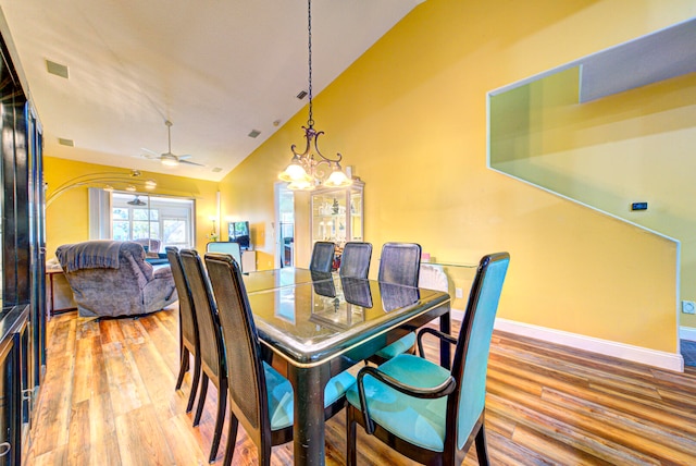 dining room featuring hardwood / wood-style flooring, ceiling fan with notable chandelier, and high vaulted ceiling