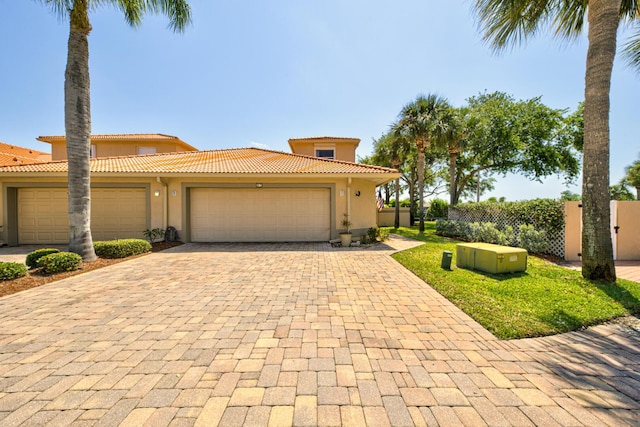 mediterranean / spanish house with a tiled roof, decorative driveway, stucco siding, a garage, and fence
