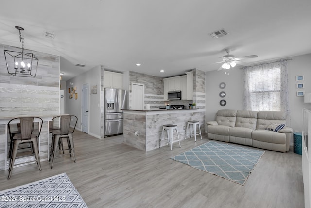 living room with ceiling fan with notable chandelier and light hardwood / wood-style floors