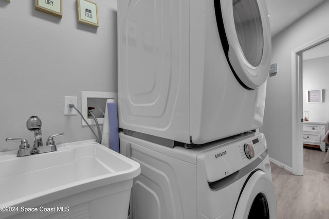 laundry room featuring sink, stacked washer and dryer, and light wood-type flooring