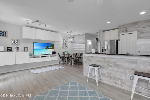 kitchen with light hardwood / wood-style floors, white cabinetry, stainless steel refrigerator with ice dispenser, and hanging light fixtures