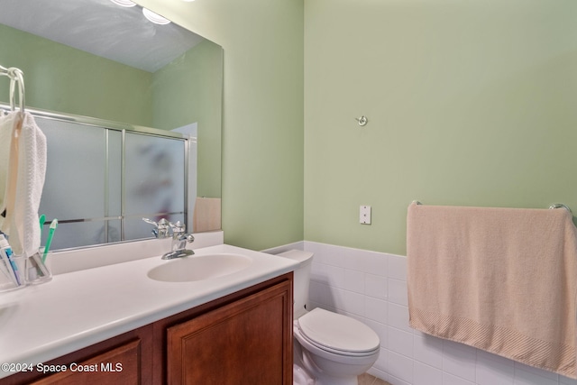 bathroom featuring vanity, toilet, a shower with door, and tile walls