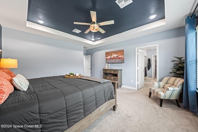 bedroom with ceiling fan, a raised ceiling, light carpet, and connected bathroom