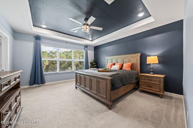 bedroom featuring a raised ceiling, ceiling fan, light colored carpet, and a textured ceiling