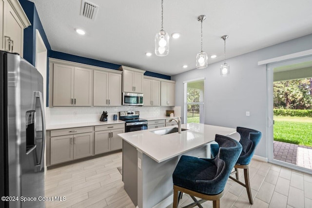 kitchen with tasteful backsplash, stainless steel appliances, sink, pendant lighting, and an island with sink