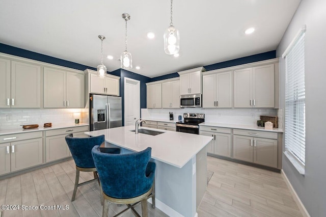 kitchen featuring a kitchen breakfast bar, sink, an island with sink, appliances with stainless steel finishes, and decorative light fixtures