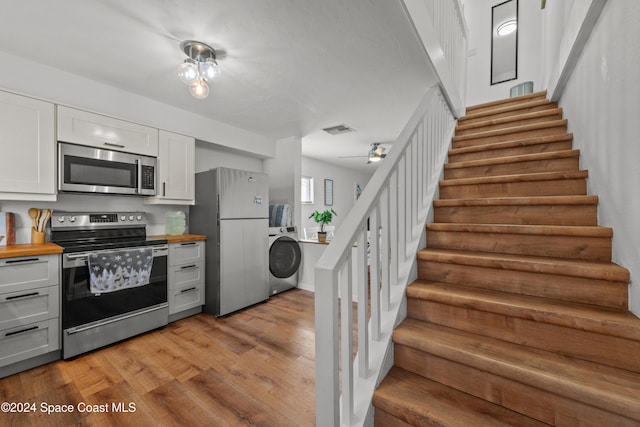 kitchen with white cabinets, light hardwood / wood-style floors, washer / dryer, butcher block counters, and stainless steel appliances