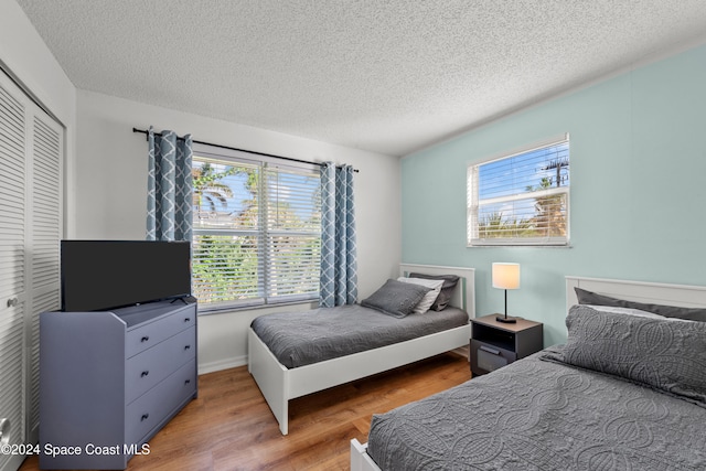 bedroom with hardwood / wood-style floors, a closet, a textured ceiling, and multiple windows