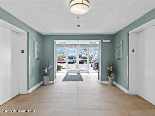 foyer with french doors, light tile patterned floors, and a textured ceiling