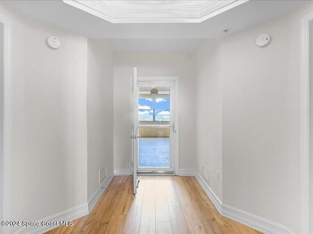 doorway to outside featuring light wood-type flooring, crown molding, and a tray ceiling