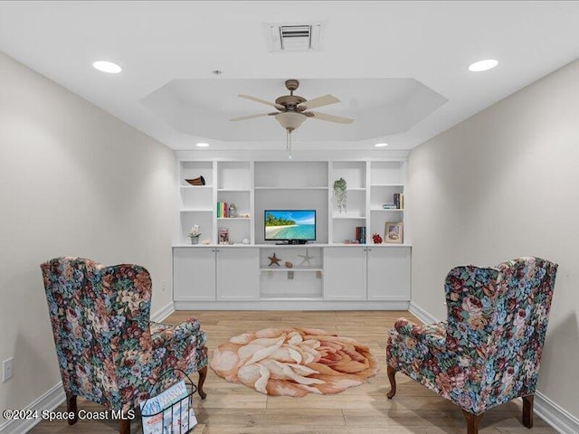 living area featuring a raised ceiling, ceiling fan, and light hardwood / wood-style flooring