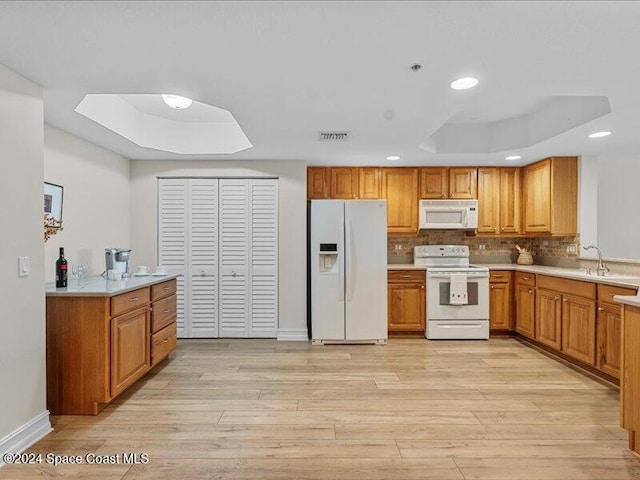 kitchen with white appliances, a tray ceiling, and light hardwood / wood-style flooring