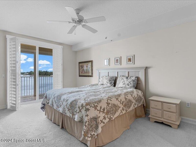 carpeted bedroom with ceiling fan, access to exterior, a textured ceiling, and a water view