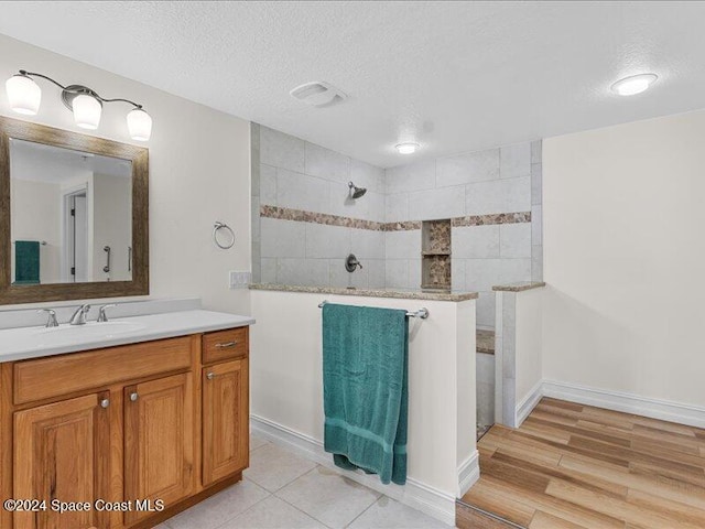 bathroom featuring hardwood / wood-style flooring, vanity, a tile shower, and a textured ceiling