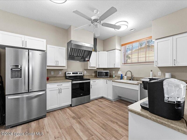 kitchen featuring white cabinets, wall chimney exhaust hood, light wood-type flooring, a textured ceiling, and stainless steel appliances