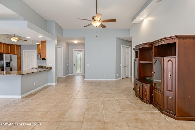 kitchen featuring kitchen peninsula, ceiling fan, light tile patterned floors, dark stone countertops, and stainless steel fridge with ice dispenser