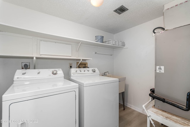 washroom with sink, washing machine and dryer, light wood-type flooring, and a textured ceiling