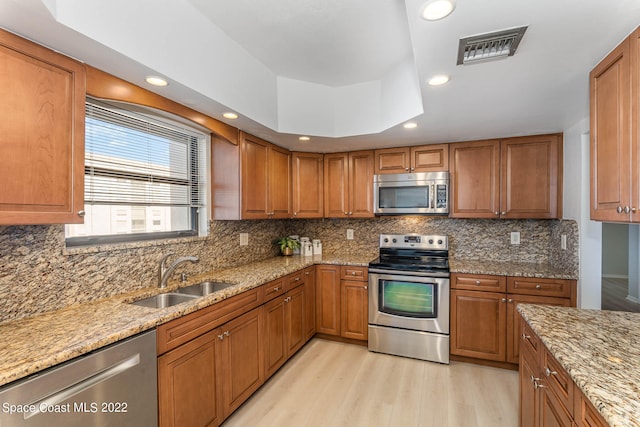 kitchen with sink, light hardwood / wood-style flooring, decorative backsplash, light stone countertops, and stainless steel appliances