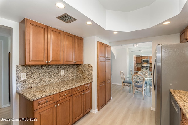 kitchen with decorative backsplash, stainless steel appliances, light hardwood / wood-style flooring, and light stone counters