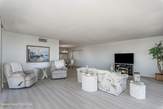 living room featuring a fireplace, a textured ceiling, light hardwood / wood-style flooring, and a notable chandelier