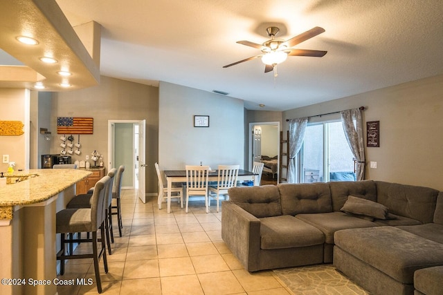 living room with ceiling fan, light tile patterned flooring, a textured ceiling, and vaulted ceiling