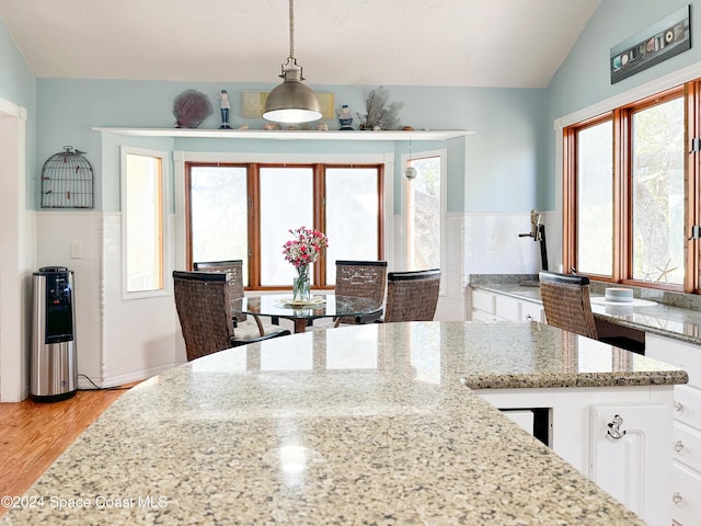 5875 Riverside Dr, Melbourne Beach, FL 32951 - kitchen featuring white cabinets, lofted ceiling, light wood-style flooring, light stone counters, and decorative light fixtures