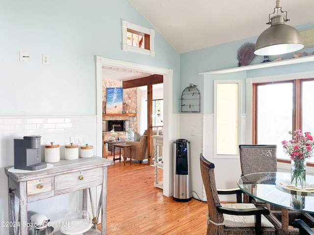 dining area with vaulted ceiling, light hardwood / wood-style flooring, and a stone fireplace