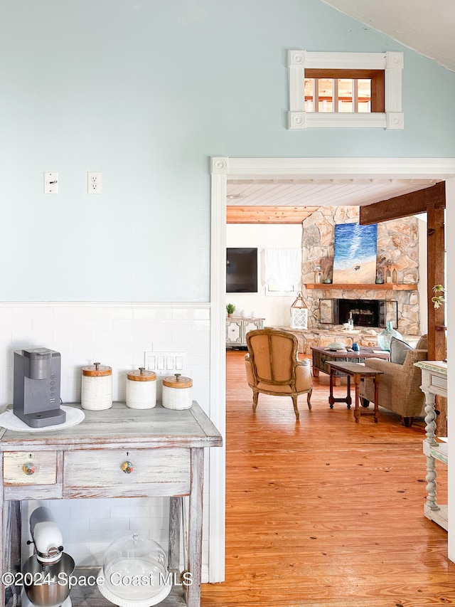 interior space with a stone fireplace, hardwood / wood-style floors, and vaulted ceiling with beams