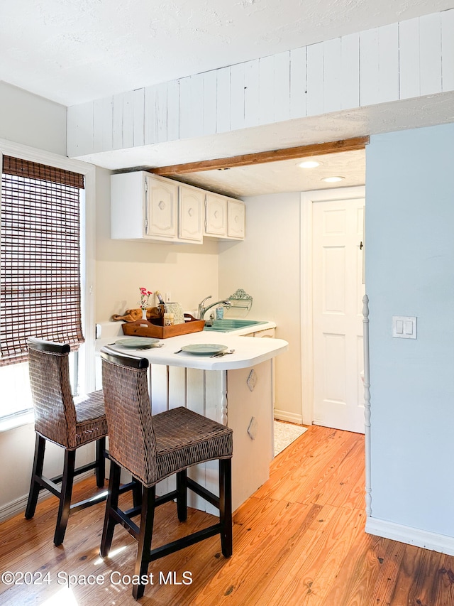 kitchen with a breakfast bar, white cabinets, sink, light hardwood / wood-style flooring, and kitchen peninsula