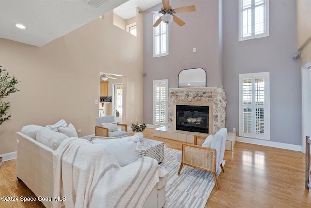 living room featuring a towering ceiling, light hardwood / wood-style floors, ceiling fan, and a tiled fireplace