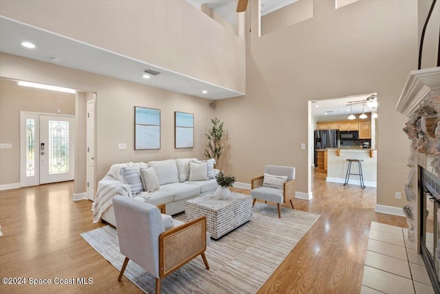 living room featuring ceiling fan, a stone fireplace, light wood-type flooring, and a towering ceiling