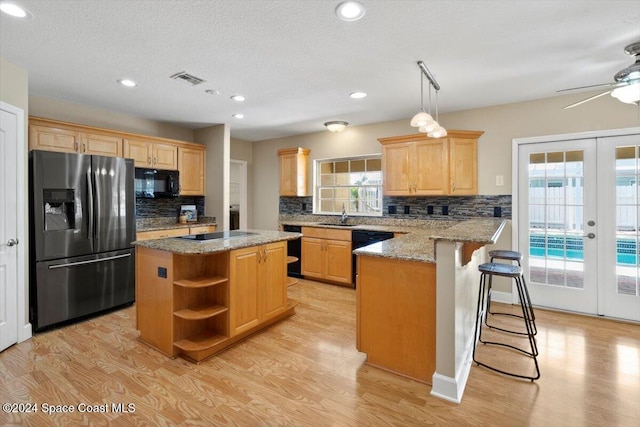 kitchen with black appliances, a center island, a healthy amount of sunlight, and light hardwood / wood-style flooring