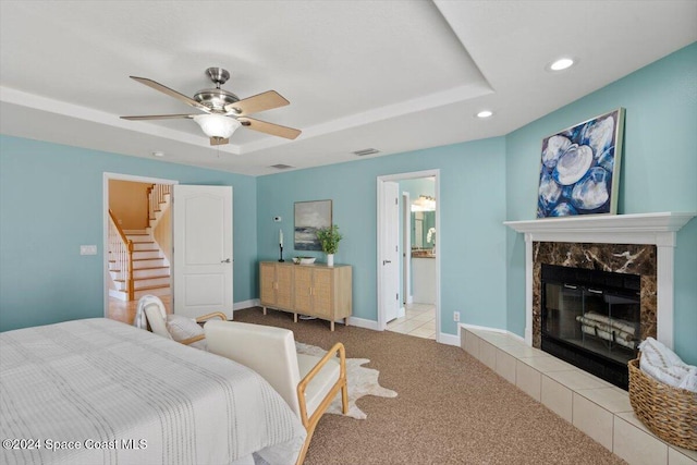 bedroom featuring ensuite bathroom, light colored carpet, ceiling fan, and a tiled fireplace