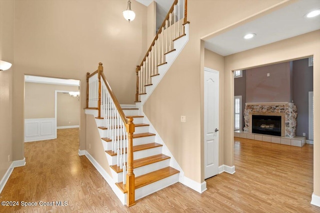 staircase with an inviting chandelier, hardwood / wood-style flooring, and a stone fireplace