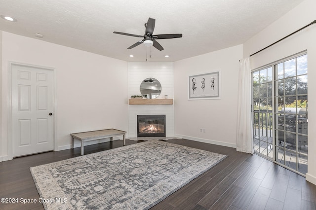 living room featuring a large fireplace, ceiling fan, dark hardwood / wood-style flooring, and a textured ceiling