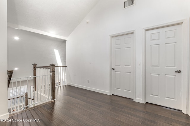 hall with a textured ceiling, high vaulted ceiling, and dark wood-type flooring