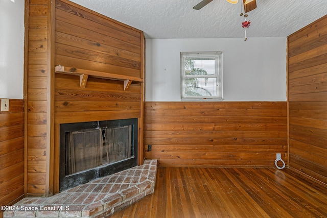 unfurnished living room with hardwood / wood-style floors, ceiling fan, a textured ceiling, and wooden walls