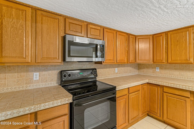 kitchen featuring tasteful backsplash, black electric range, light tile patterned floors, and a textured ceiling