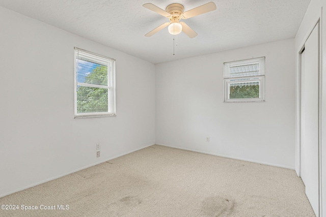 carpeted spare room with ceiling fan, plenty of natural light, and a textured ceiling