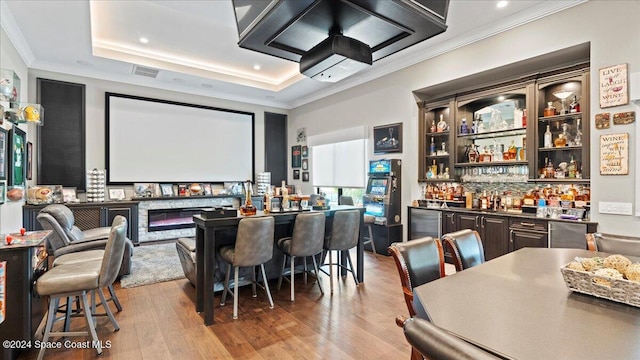 home theater room featuring a raised ceiling, bar, light hardwood / wood-style floors, and ornamental molding