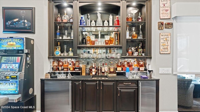 bar featuring dark brown cabinetry, stainless steel fridge, and dark stone counters