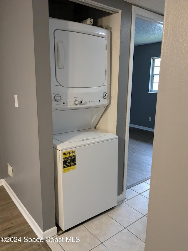 laundry area featuring light tile patterned flooring, a textured ceiling, and stacked washer and clothes dryer