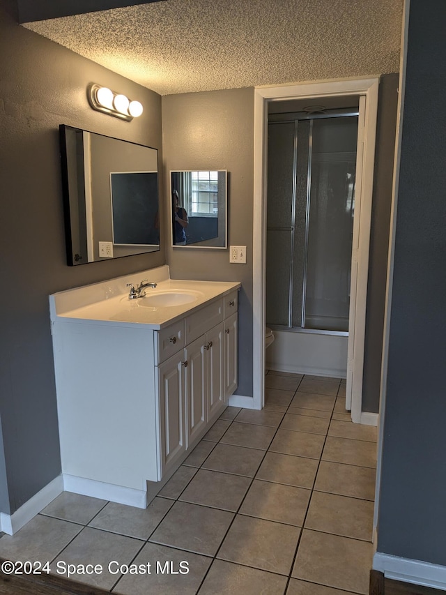 bathroom with tile patterned floors, vanity, bath / shower combo with glass door, and a textured ceiling